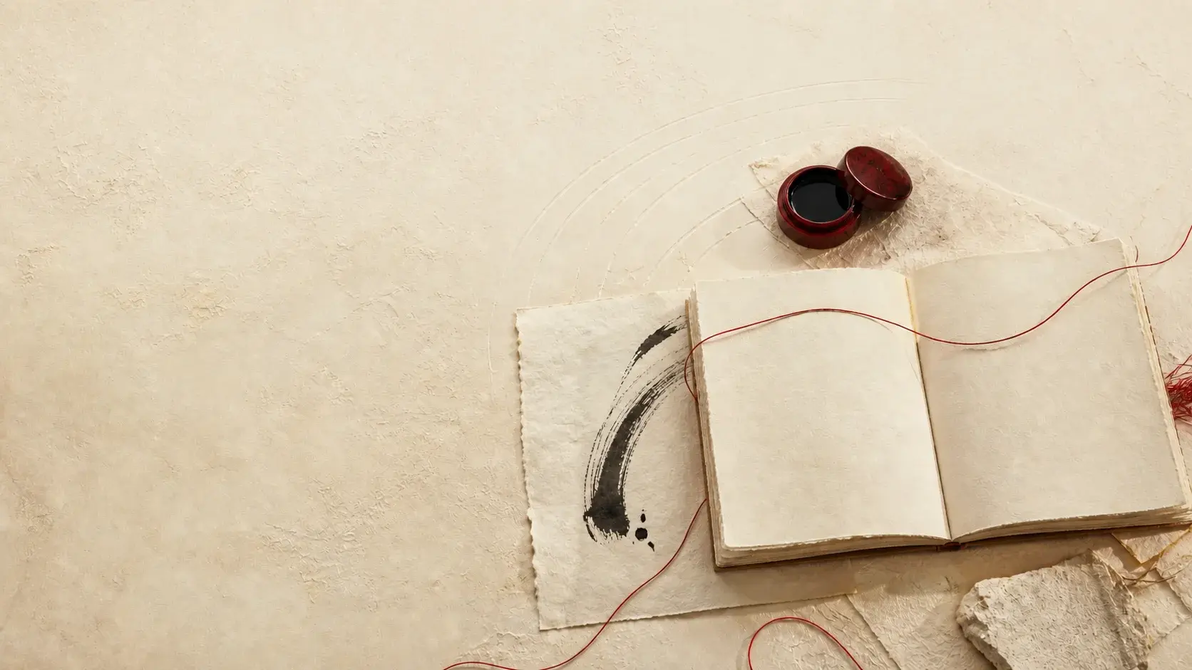 Cuaderno abierto, tinta y papeles artesanales unidos por un hilo rojo